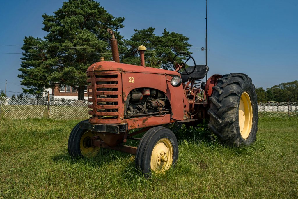 A vintage tractor sits in a sunny field in Angliers, Quebec, Canada, capturing rural life.