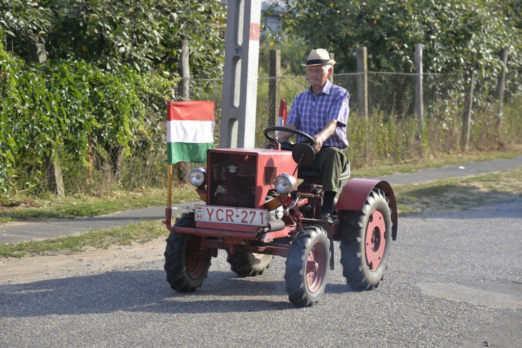 T25 – Vello Senior man drives a red vintage tractor with Hungarian flag in Nyírmada.