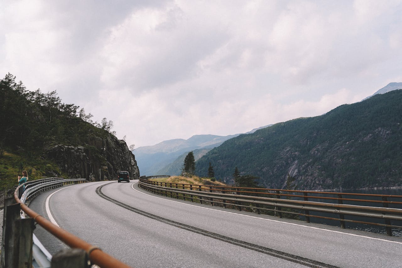 Avaleht A picturesque road curves along a mountain cliffside under a cloudy sky, ideal for travel and adventure themes.