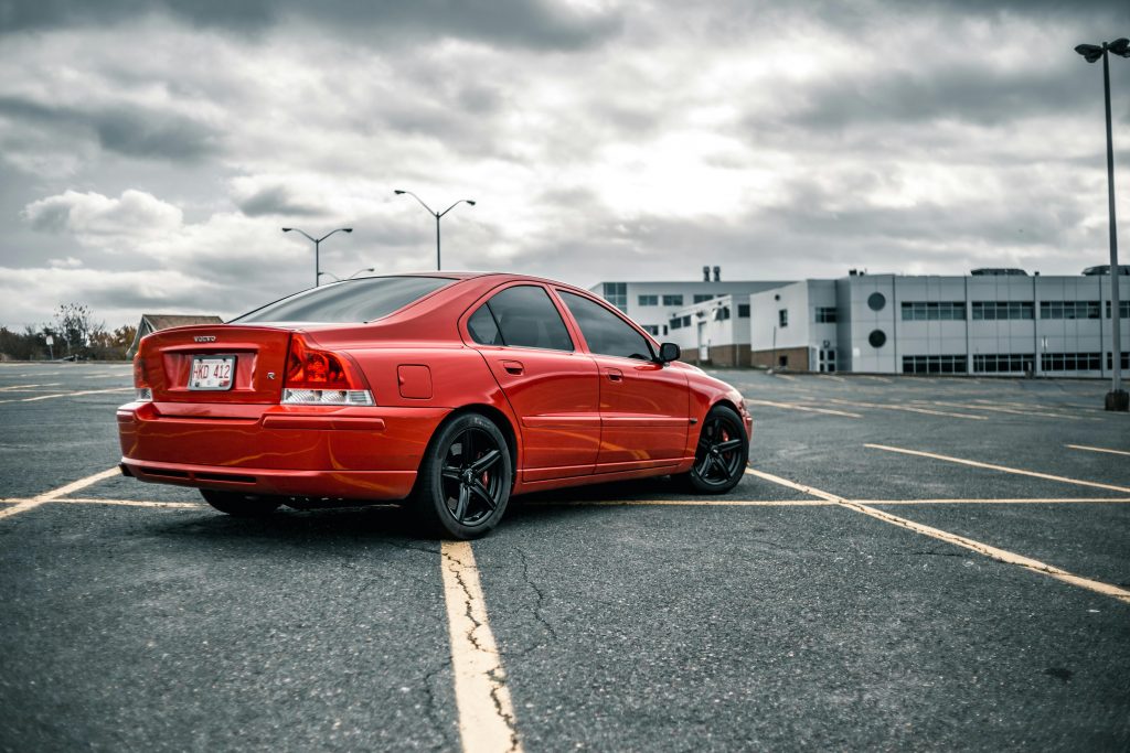 Volvo S60 – Ivar & Taivo A red Volvo car parked in an empty lot under a cloudy sky, showcasing modern automotive design.