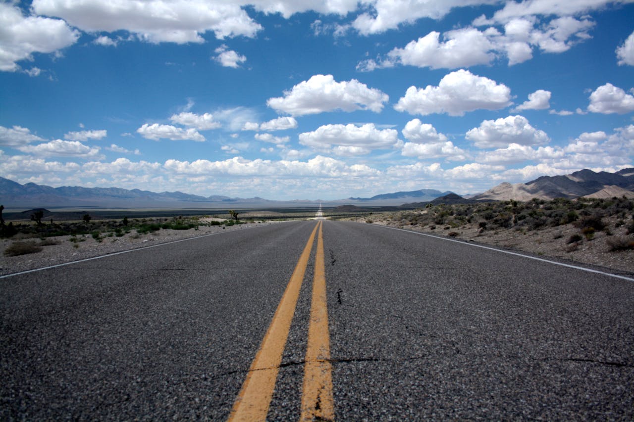 Avaleht A straight road stretches into the desert horizon under a cloud-filled blue sky.